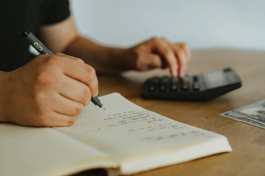 A person writing in a notebook next to a calculator