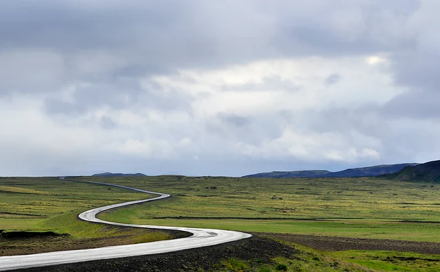 A winding road through a green landscape under a cloudy sky.