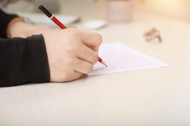 A person's hand filling out an answer sheet with a pencil.