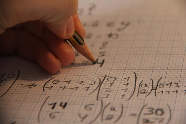 A hand writing mathematical equations on graph paper with a pencil.