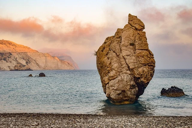 A large rock formation in the sea with cliffs in the background.