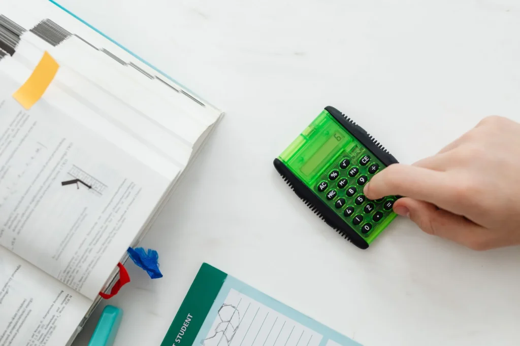 A person using a calculator next to an open textbook.