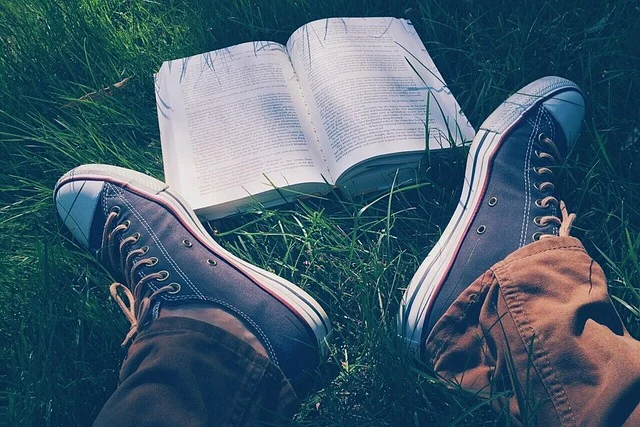 A person relaxing in grass with an open book and wearing sneakers.