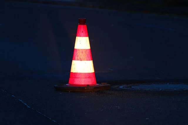A red and white striped traffic cone on a dark road.