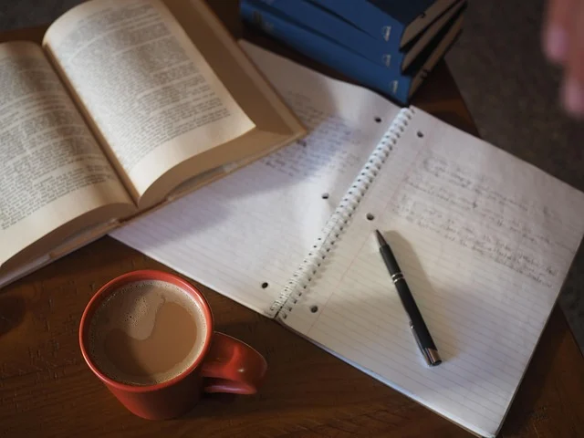 An open textbook, notebook, pen, and coffee mug on a desk