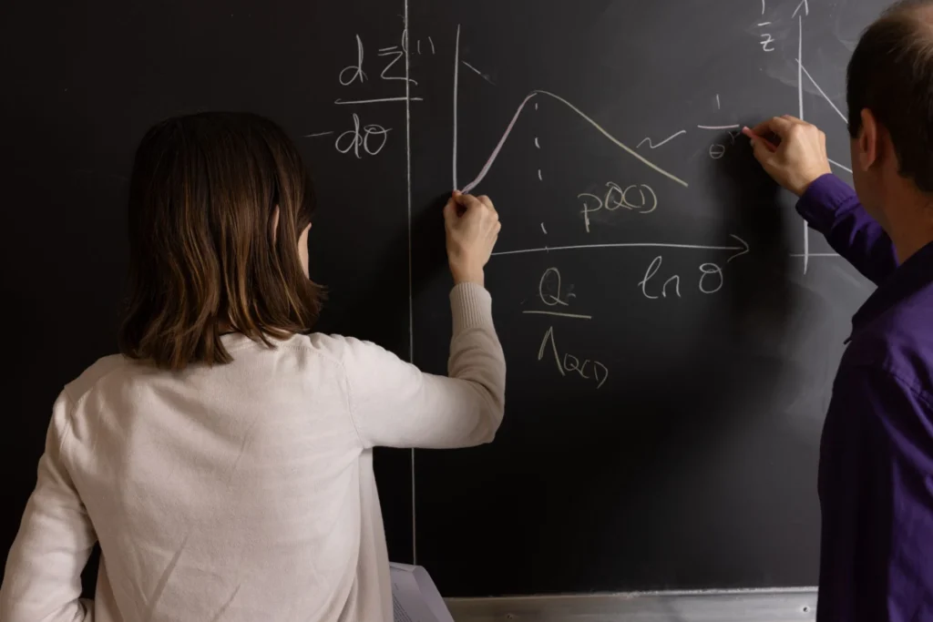 Two people drawing mathematical graphs and writing equations on a blackboard
