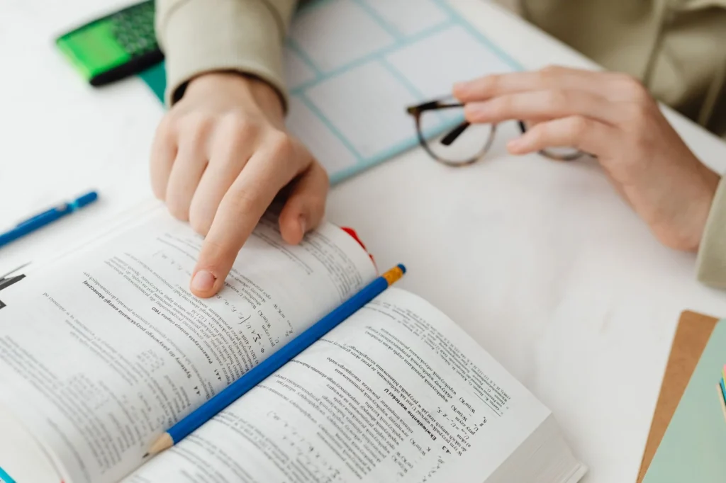 Matrix multiplication: A person pointing at a textbook with mathematical formulas and equations.