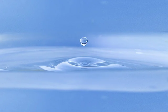 A single water droplet falling into a body of water, creating ripples.