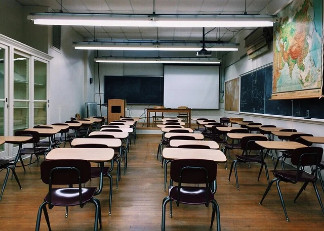 An empty classroom with desks, chairs, blackboards, and a projector screen.