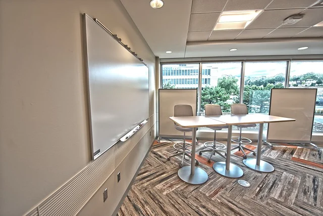 An empty conference room with a whiteboard, tables, and chairs.