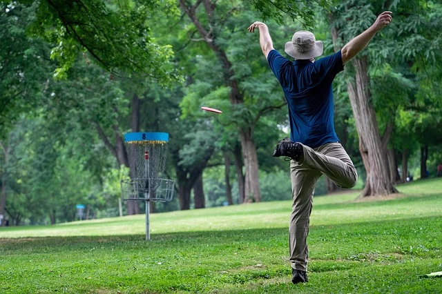 A person throwing a disc golf disc towards a basket.