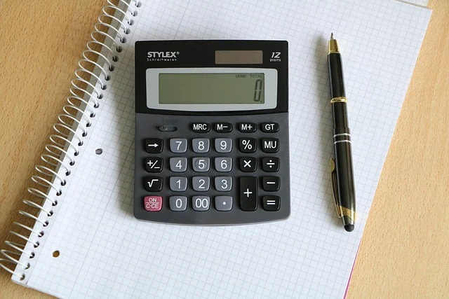 A calculator, pen, and notebook on a wooden desk.
