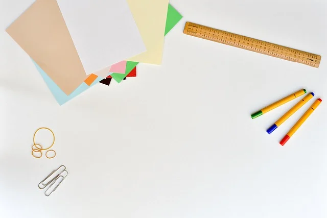 Colorful paper, a wooden ruler, markers, and paperclips on a desk