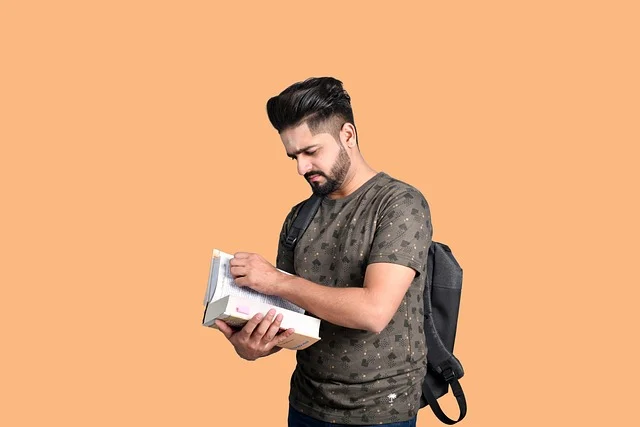 A young man with a backpack reading a book, possibly studying.