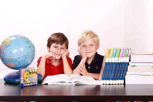 Two young boys sitting at a desk with books and a globe