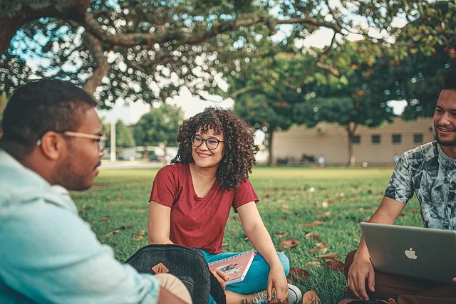 Three students sitting on grass studying together with a laptop