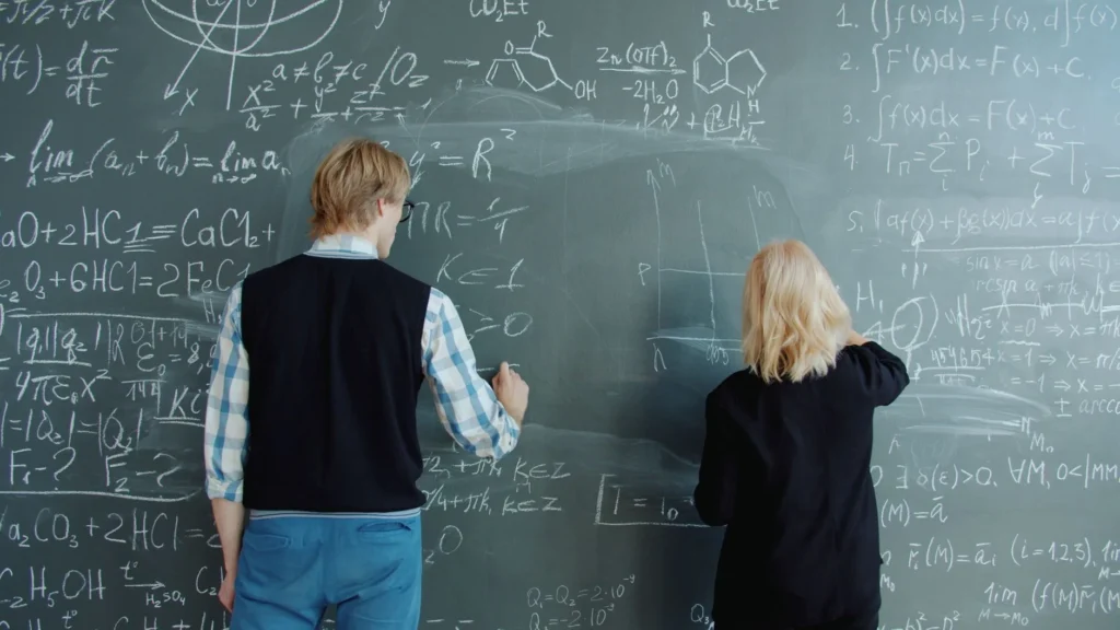 Differential equations: Two people writing complex math and science equations on a blackboard