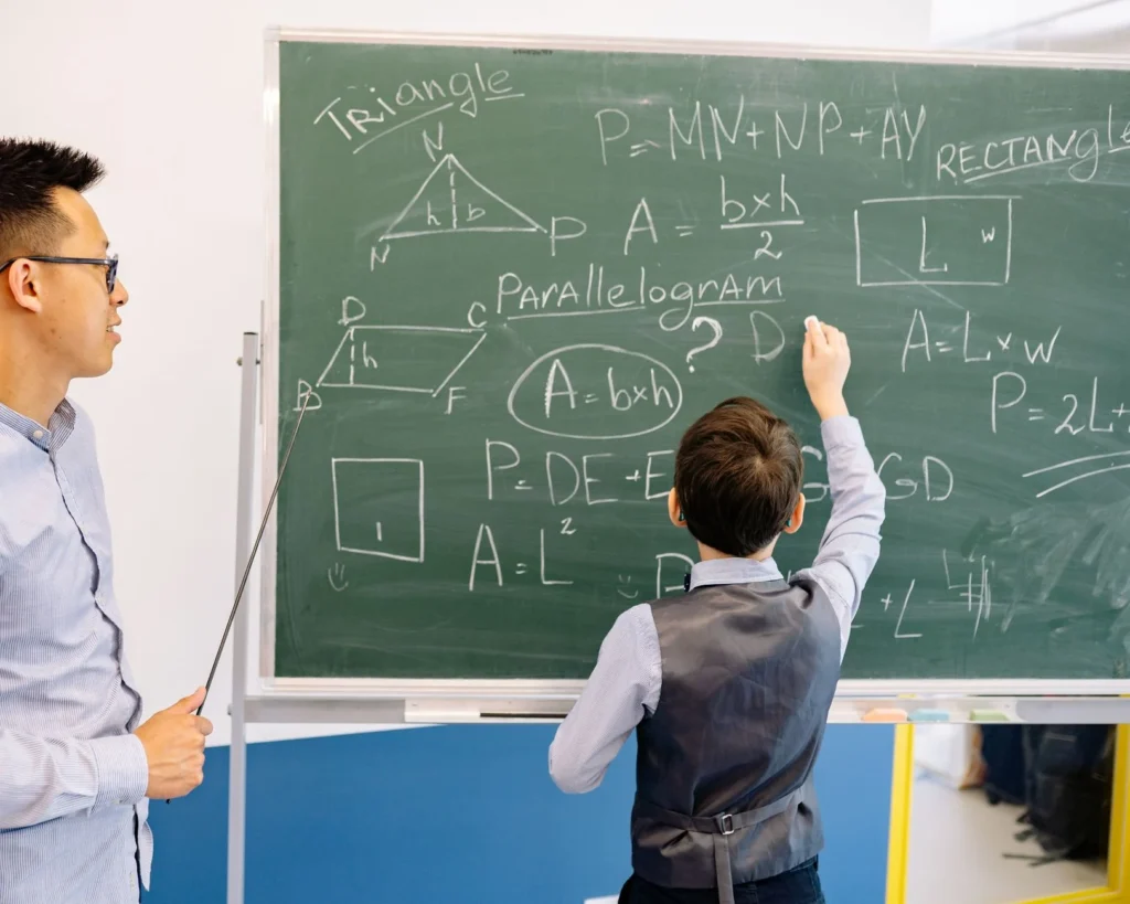 A teacher watching a student write math formulas on a chalkboard