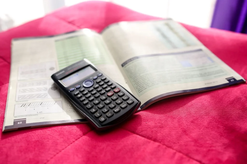 A scientific calculator on an open textbook, resting on a pink surface.