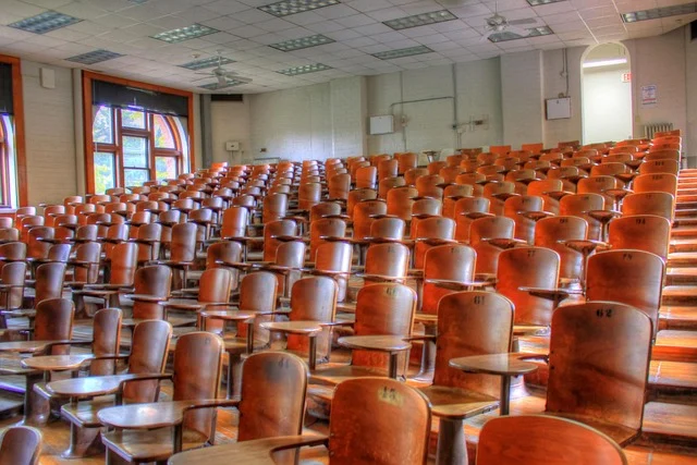 An empty lecture hall with rows of wooden desks and chairs.