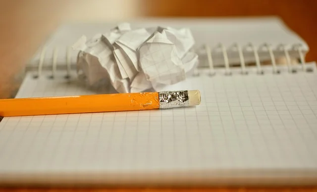 A pencil, crumpled paper, and a spiral-bound graph paper notebook.