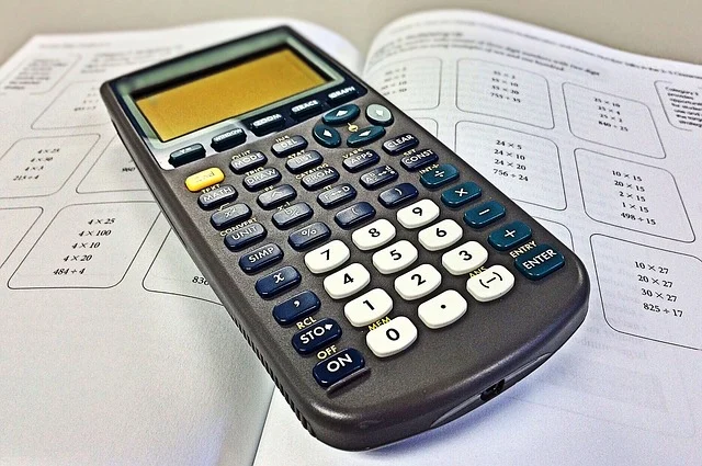 A scientific calculator on top of a math textbook with problems.