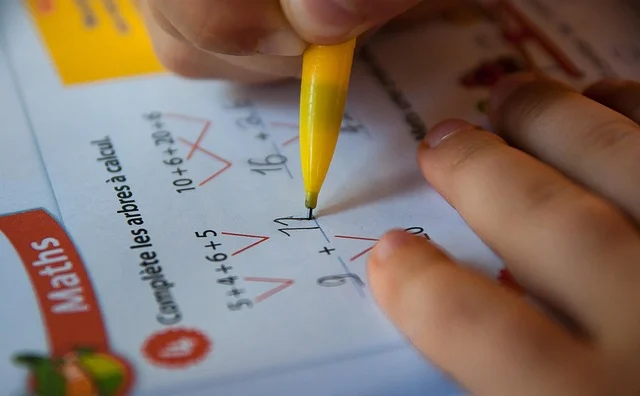 A child writing simple math addition equations on a worksheet