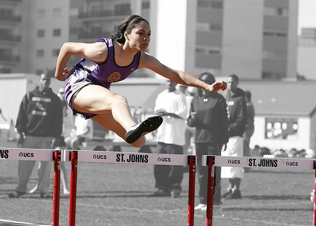 A female athlete jumping over hurdles during a track and field event.