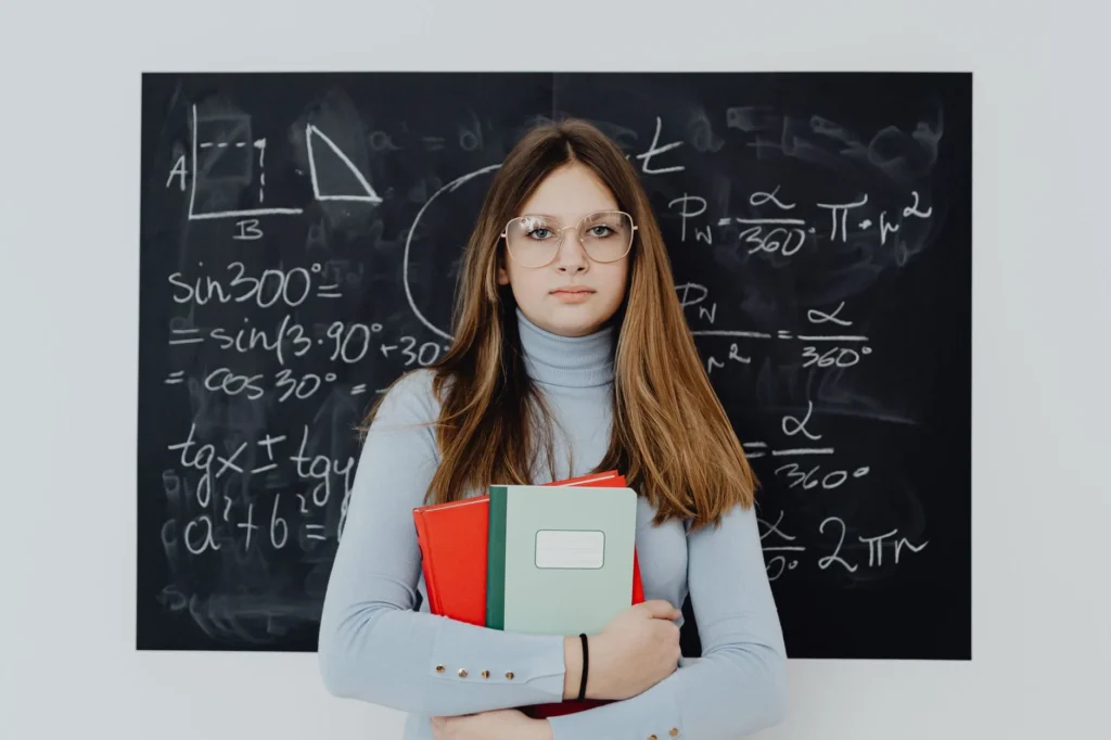 A student with books in front of a blackboard with math equations.