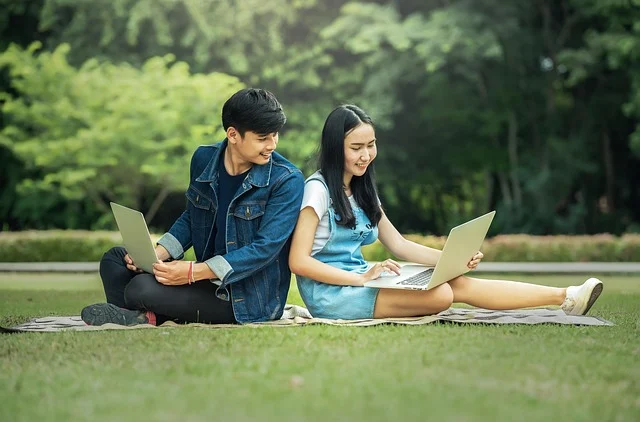 Free calculus textbook pdf: Two students sitting outdoors studying on laptops back-to-back